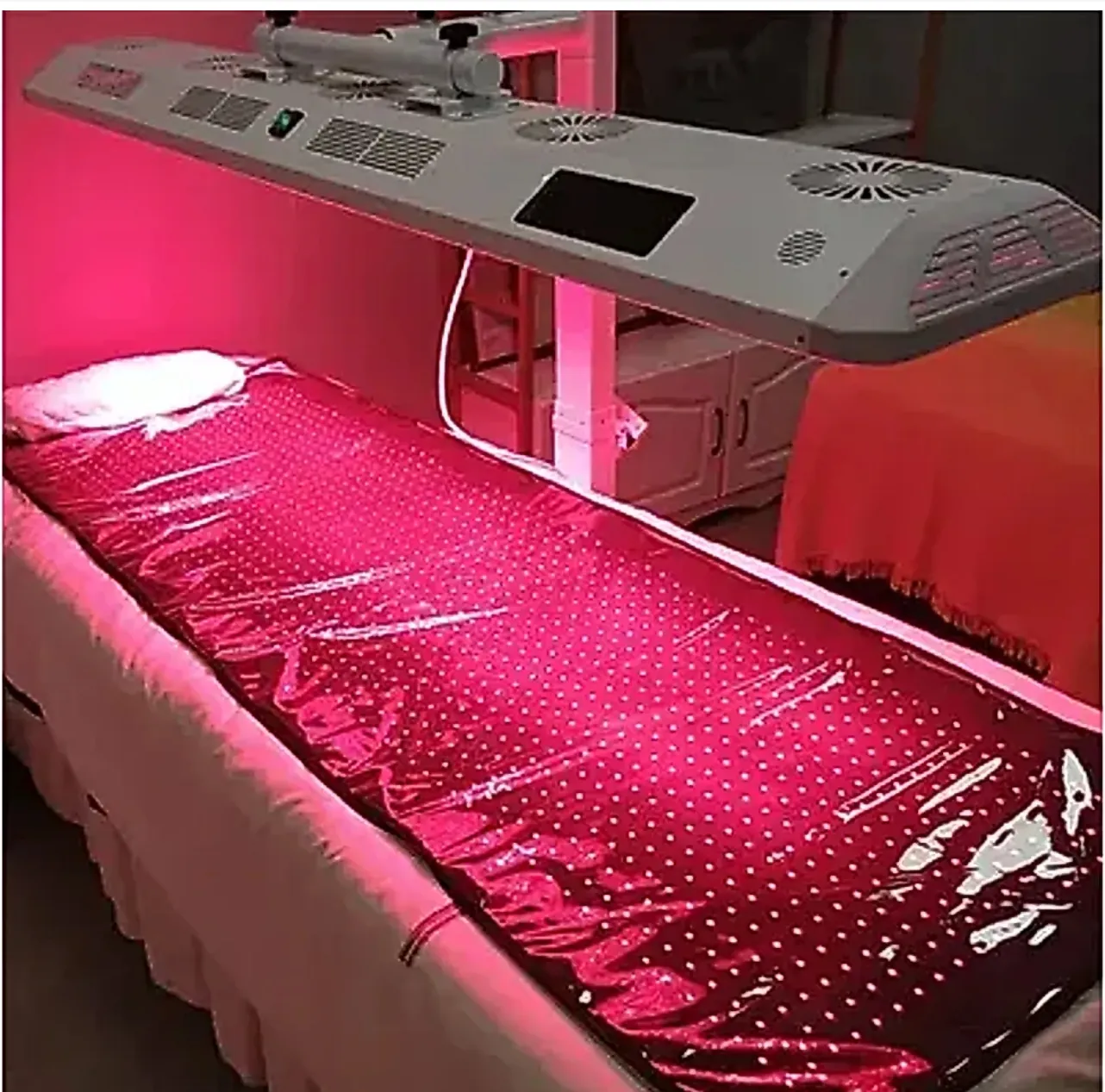 Treatment bed covered with a glowing red LED mat, with a large red light device mounted overhead